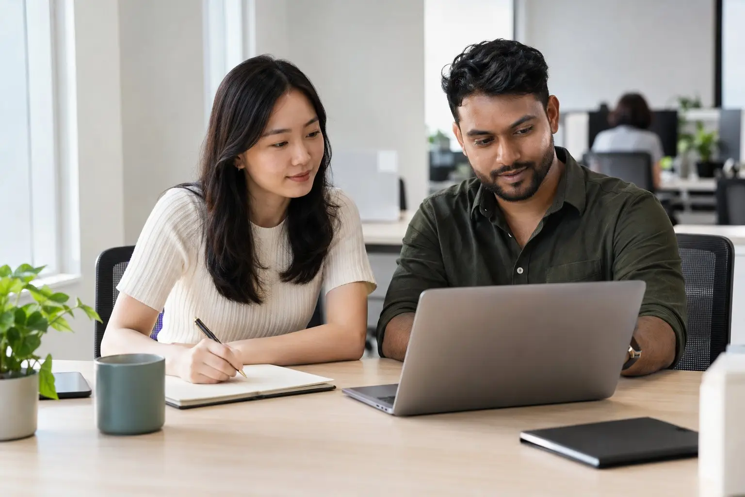 Two colleagues comparing notes over a laptop at an ordinary office desk